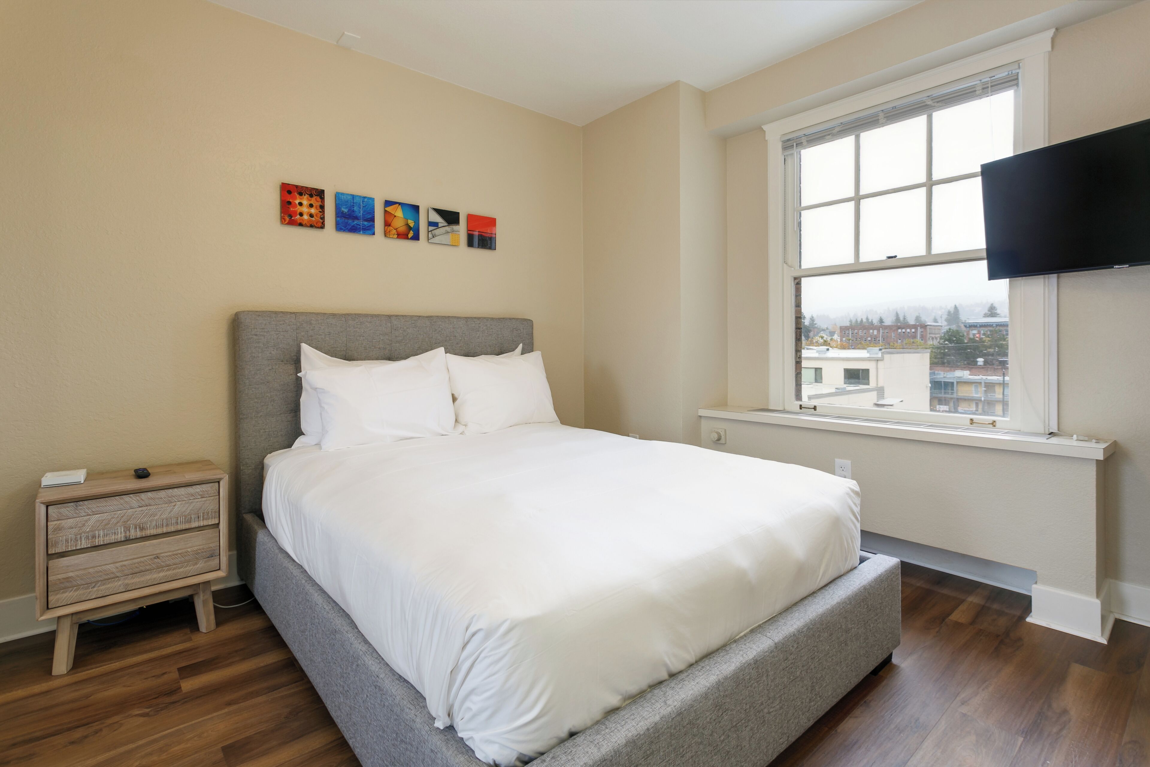 Un dormitorio con cama, mesita de noche, ventana con vistas y televisor de pantalla plana montado en la pared.
