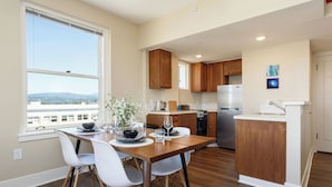 A modern kitchen with wooden cabinets, a dining area with a table and chairs, and a view of the city through a large window. - Hotel Leo (Bellingham)