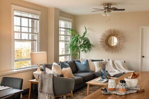 A living room with a sofa, coffee table, and a dining table. There is a plant, a lamp, and a mirror on the wall.