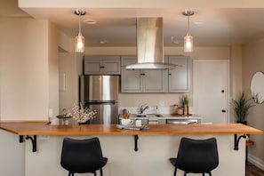A modern kitchen with a central island, stainless steel appliances, pendant lighting, and black chairs.