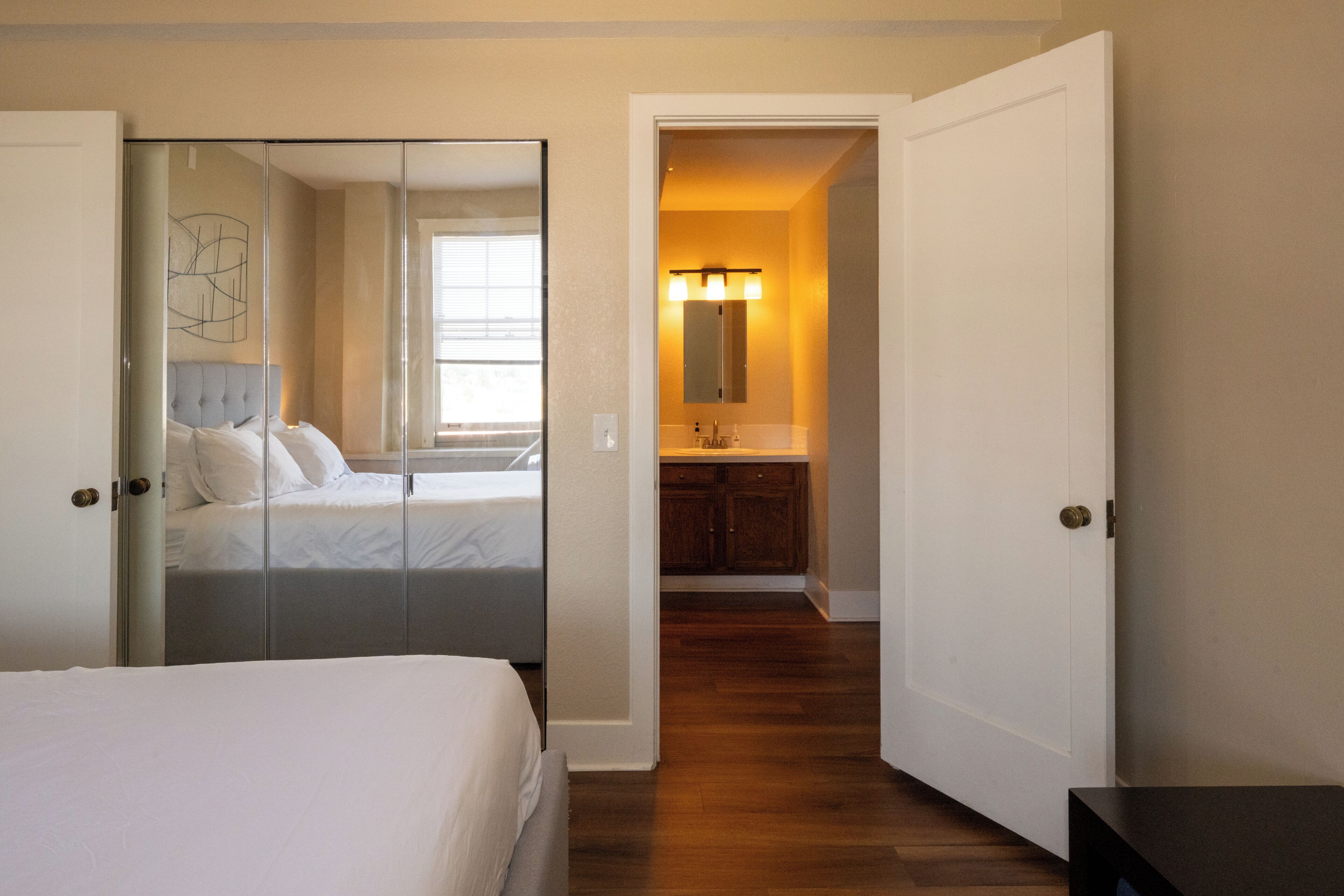 A hotel room with a bed, a walk-in closet, a bathroom with a mirror and sink, and a hallway leading to another room.