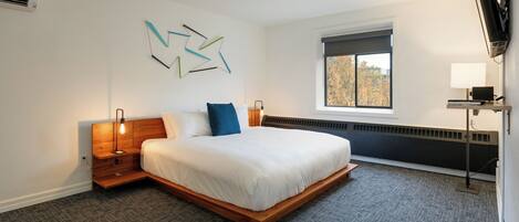 Una habitación de hotel moderna con una cama grande, un escritorio con ordenador, una ventana con vistas y un televisor montado en la pared.