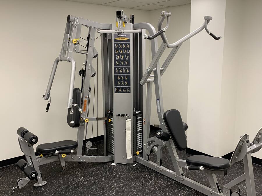 Uma academia com diversos equipamentos de exercícios, incluindo um aparelho de supino, leg press e puxada alta.