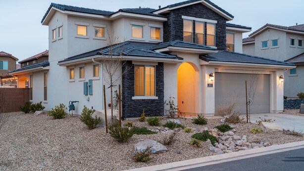 Une maison moderne à deux étages, dotée d’une façade en pierre, d’un garage et d’un jardin bien entretenu avec du gravier et de petites plantes.