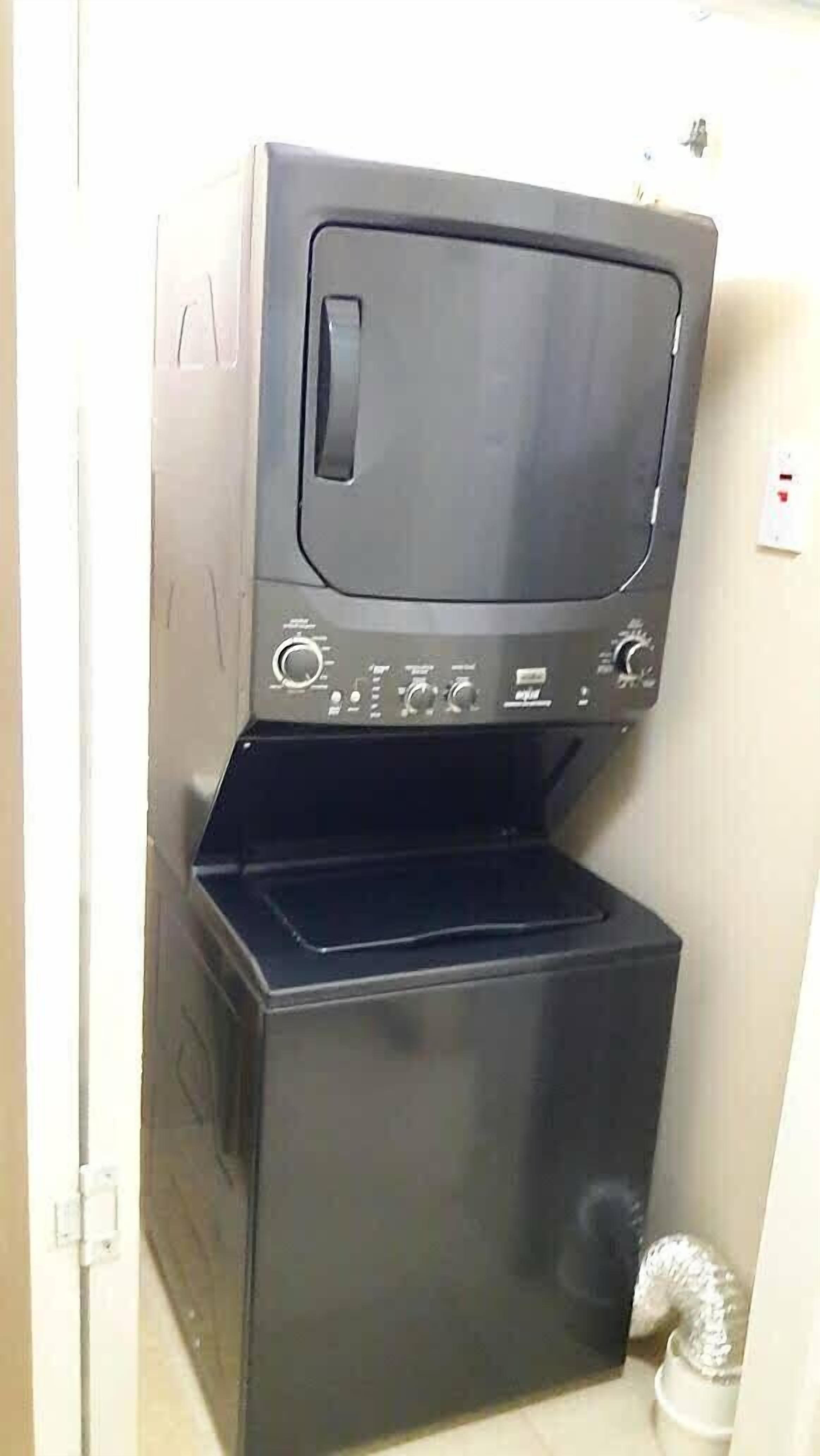 Una lavadora compacta de color oscuro con un panel de control y un pequeño compartimento de almacenamiento debajo.