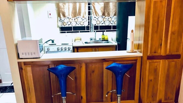 A kitchen with wooden cabinets, a stove, and a sink. There are two blue bar stools and a vase with yellow flowers on the counter. - Waterloo Executive Guest Apartment (Kingston)