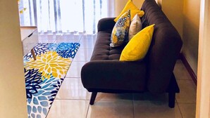 A living room with a sofa, yellow cushions, a floor lamp, and a patterned rug. - Waterloo Executive Guest Apartment (Kingston)