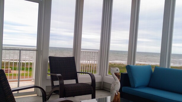 A covered outdoor seating area with wicker chairs, a blue sofa, and a small table. - Ocean Front Cottage. (Cable Head East)