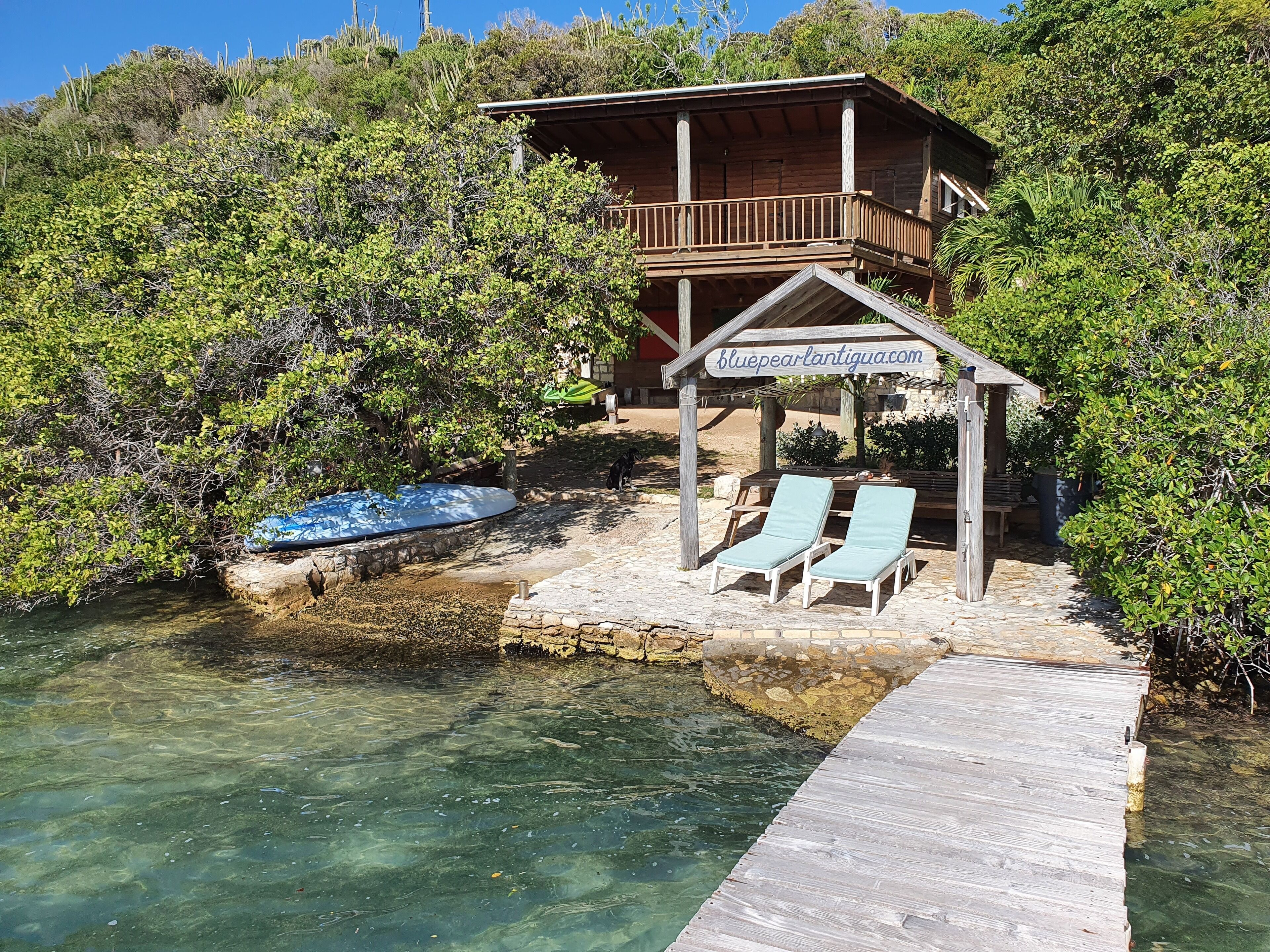 A wooden cabin with a balcony and a sign reading "bluepearlantigua.com".