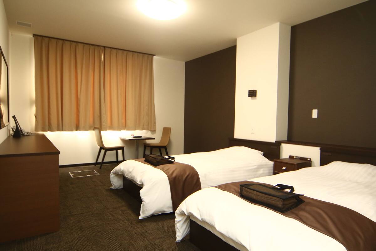 A hotel room with two beds, a desk, a chair, and a small table.