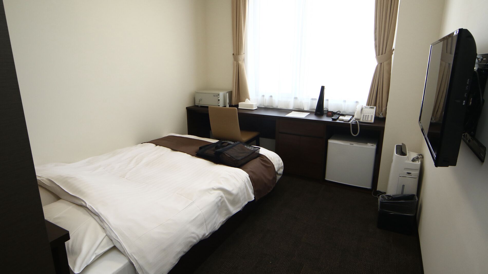 A hotel room with a bed, desk, chair, and a small refrigerator.