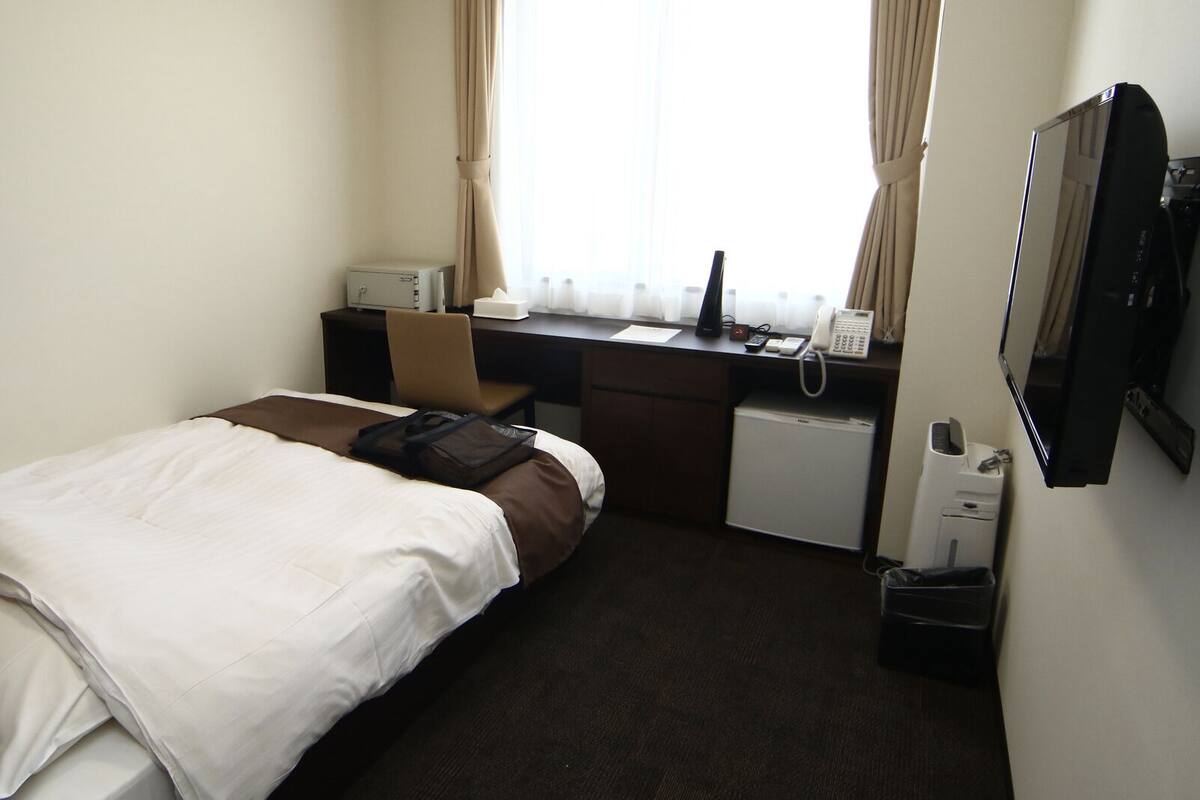 A hotel room with a bed, desk, chair, and a small refrigerator.