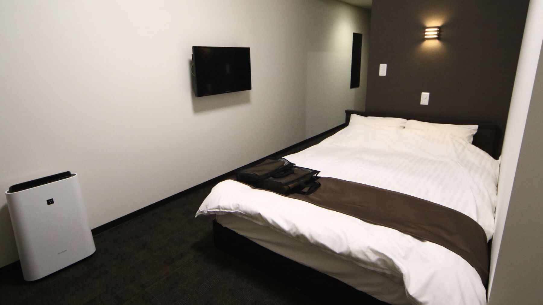 A hotel room with a bed, a flat-screen TV mounted on the wall, and a compact air purifier.