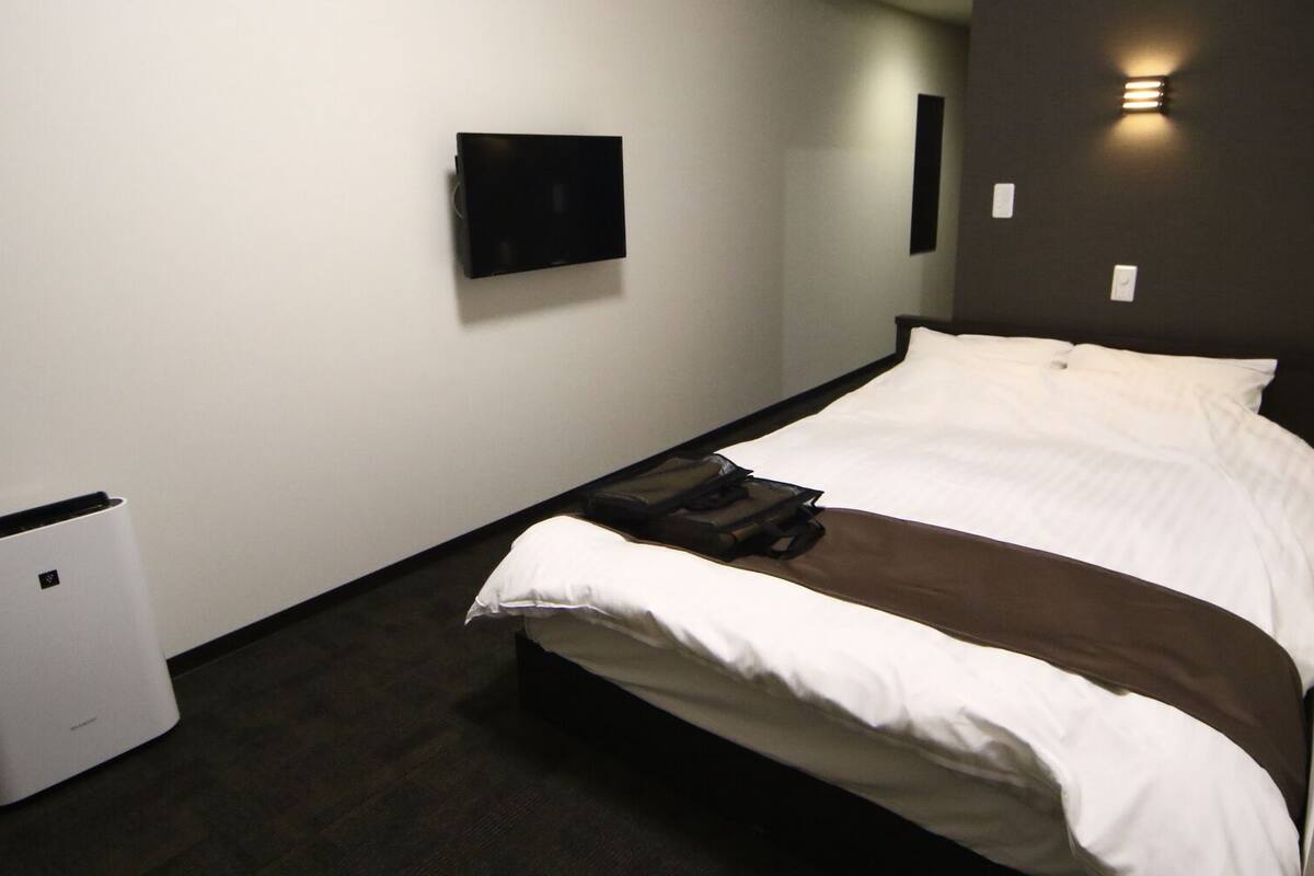 A hotel room with a bed, a flat-screen TV mounted on the wall, and a compact air purifier.
