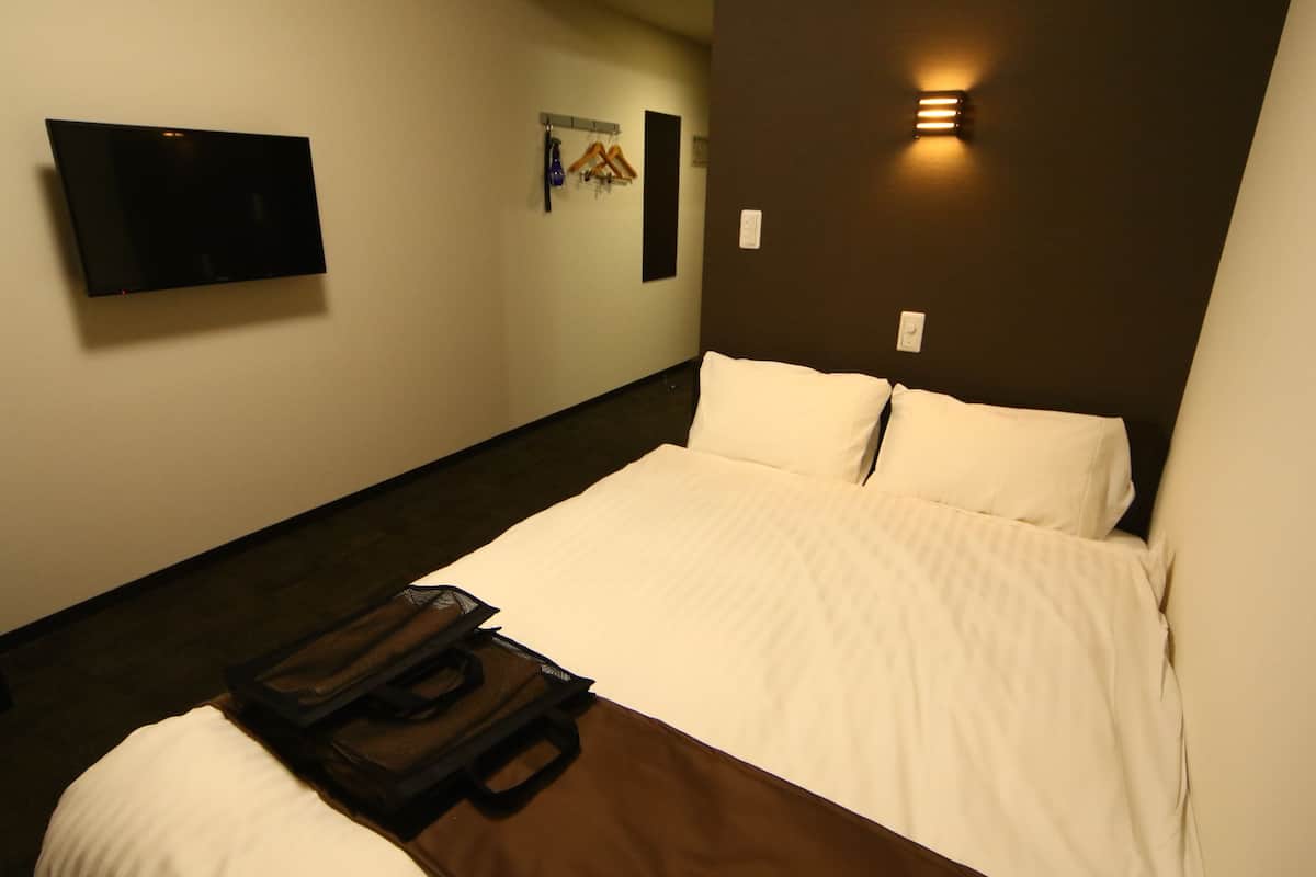 A hotel room with a bed, a flat-screen TV mounted on the wall, and a wall-mounted light fixture.