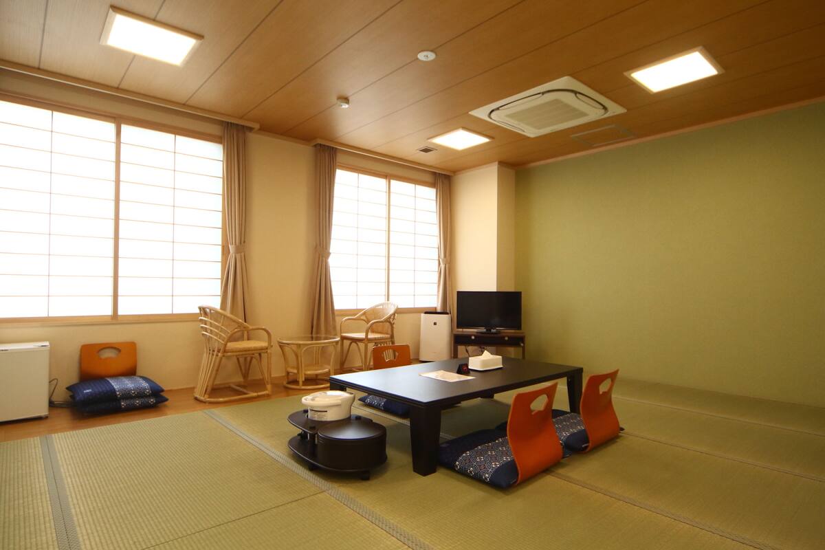 A room with tatami mats, a tatami mat table, a television, and a futon bed.