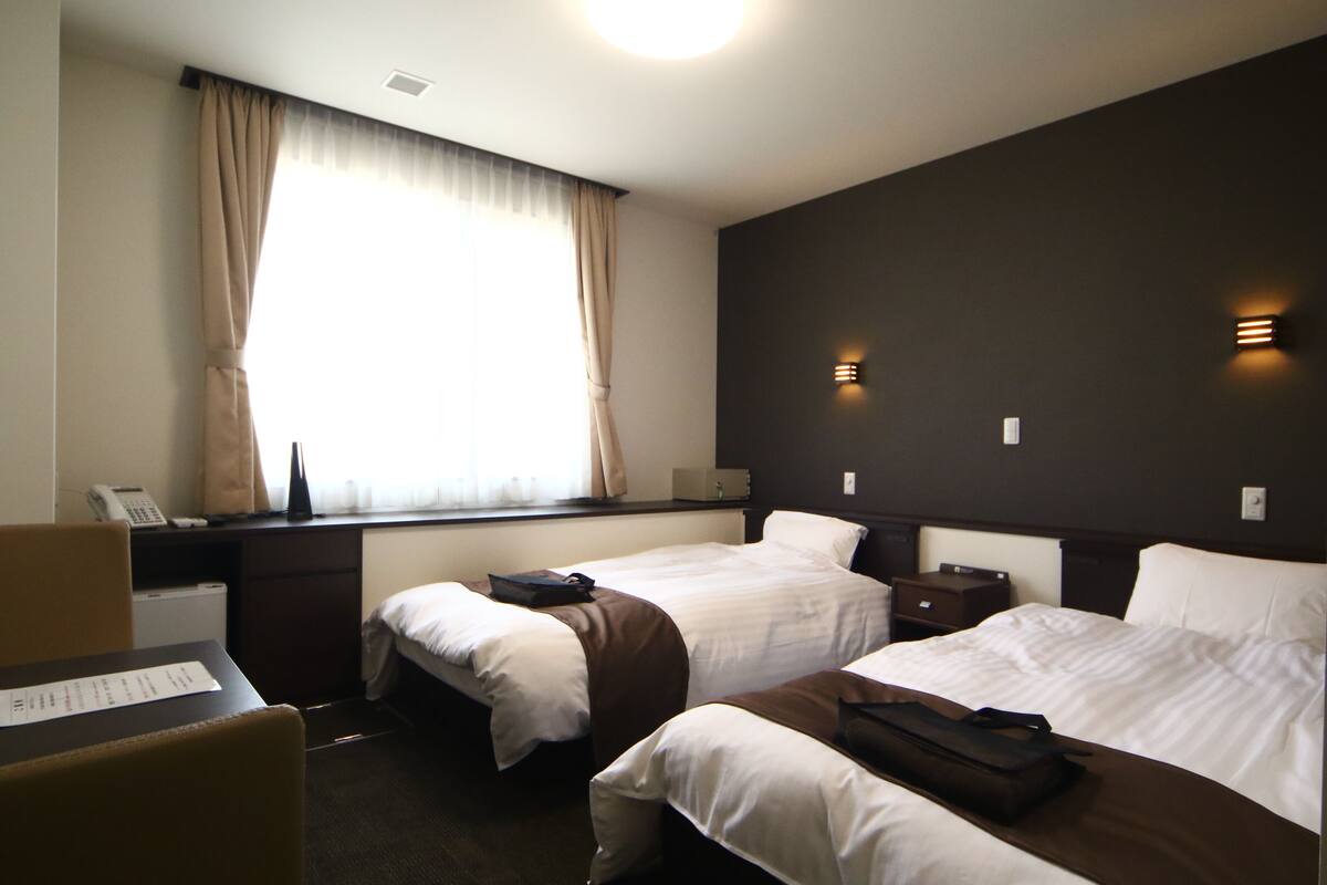 A hotel room with two beds, a desk with a telephone, and a window with curtains.