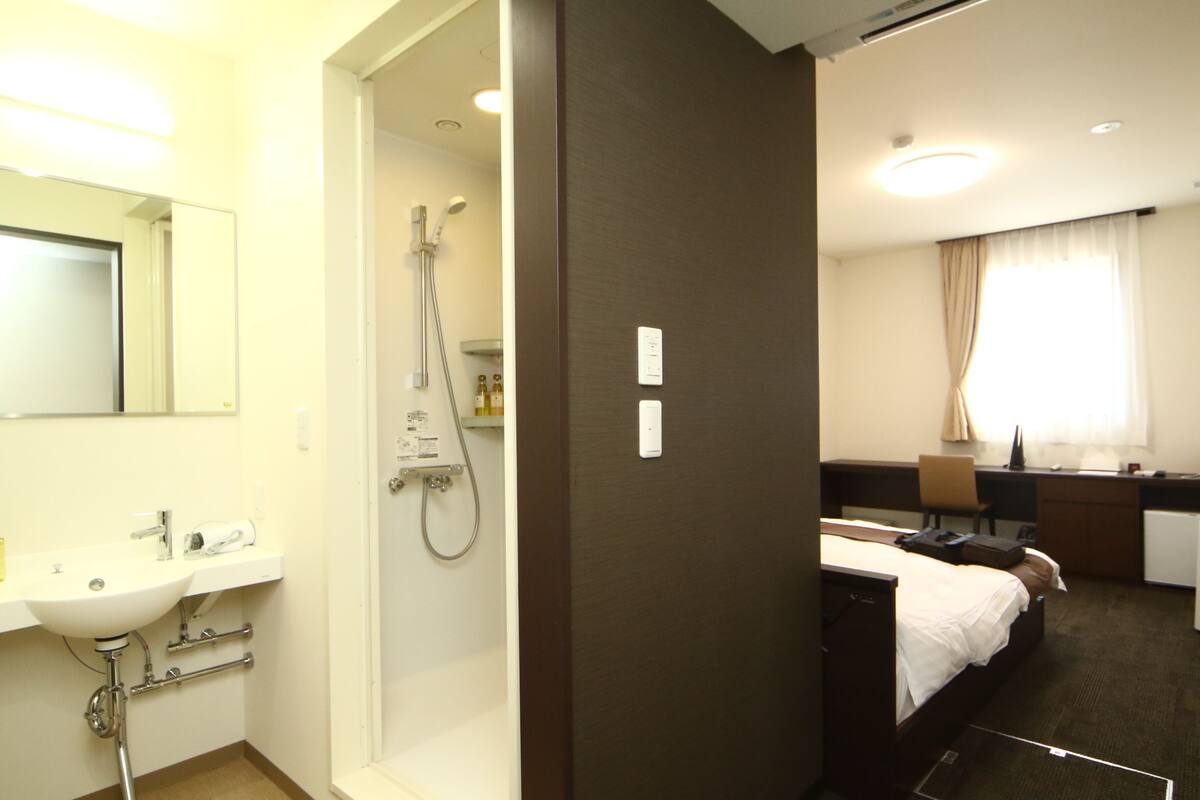 A hotel room with a bathroom, a desk, a bed, and a window with curtains.