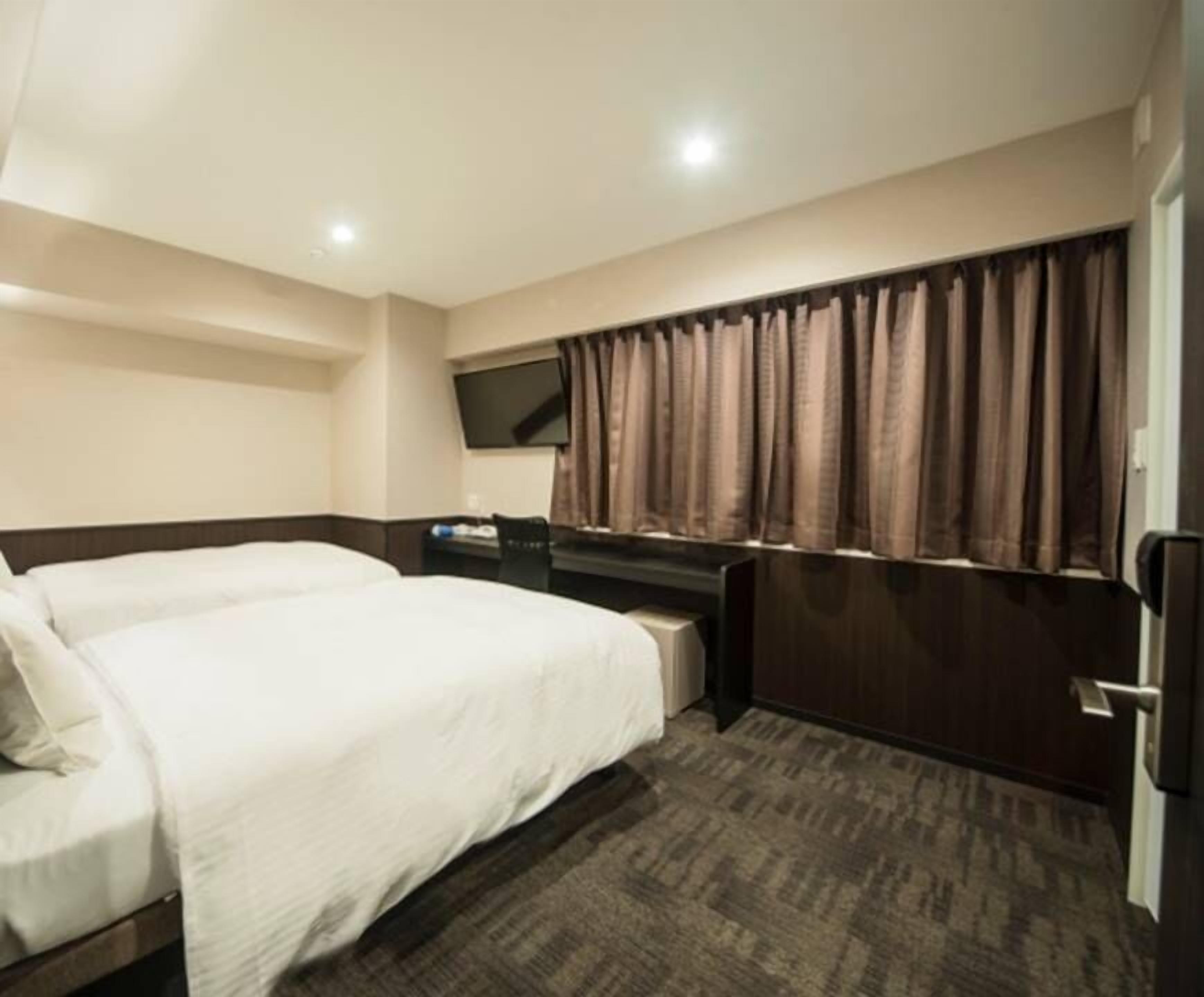 Quarto de hotel com duas camas, uma escrivaninha, televisão e janela com cortinas.