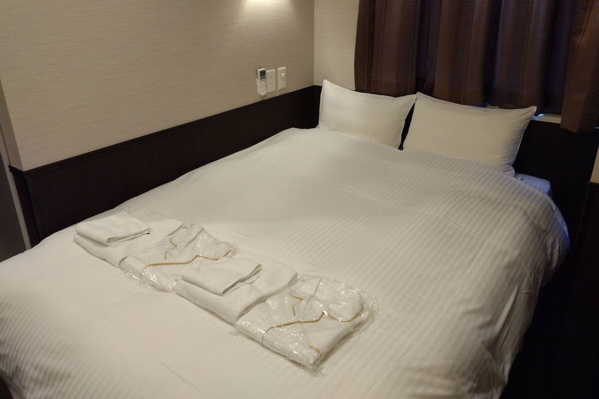 A neatly made bed with white linens, a headboard, and a wall-mounted light fixture.