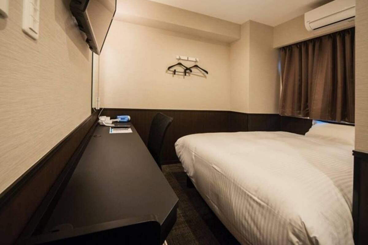 A hotel room with a bed, a desk, and a TV mounted on the wall.