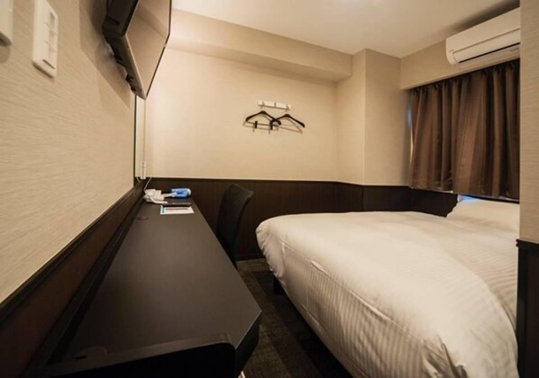 Una habitación de hotel con cama, escritorio y televisor montado en la pared.