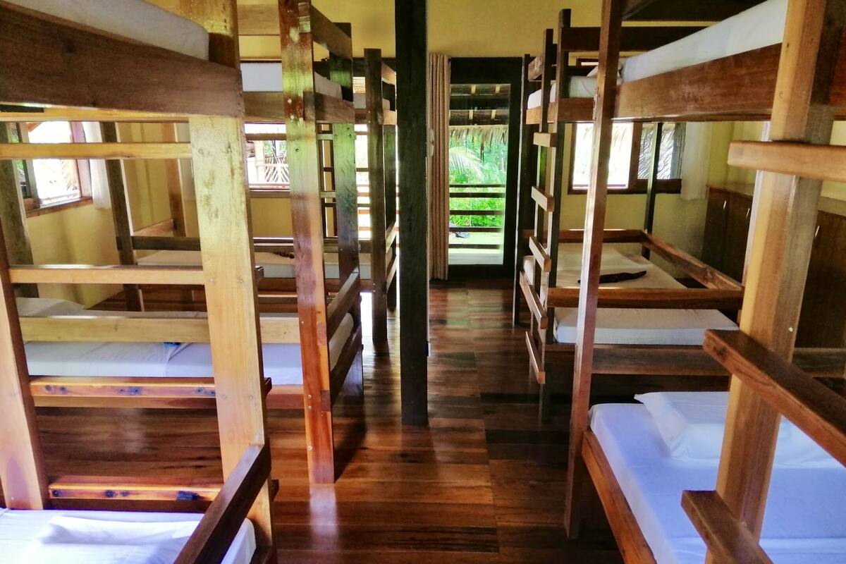 A row of bunk beds with wooden frames and white bedding, arranged in a corridor with a wooden floor.