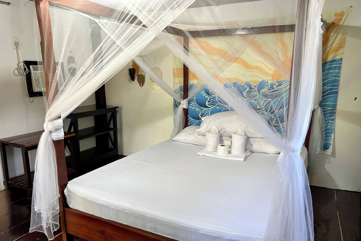 A bed with a canopy, a bedside table, a wall with a decorative pattern, and a power outlet.