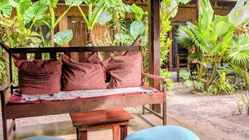 A wooden bench with patterned cushions, surrounded by tropical plants and a thatched roof structure.