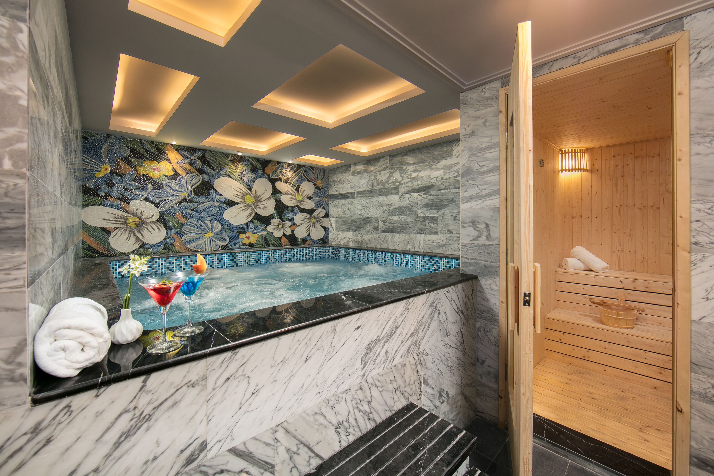 A modern bathroom with a marble sink, a jacuzzi, and a wooden sauna.