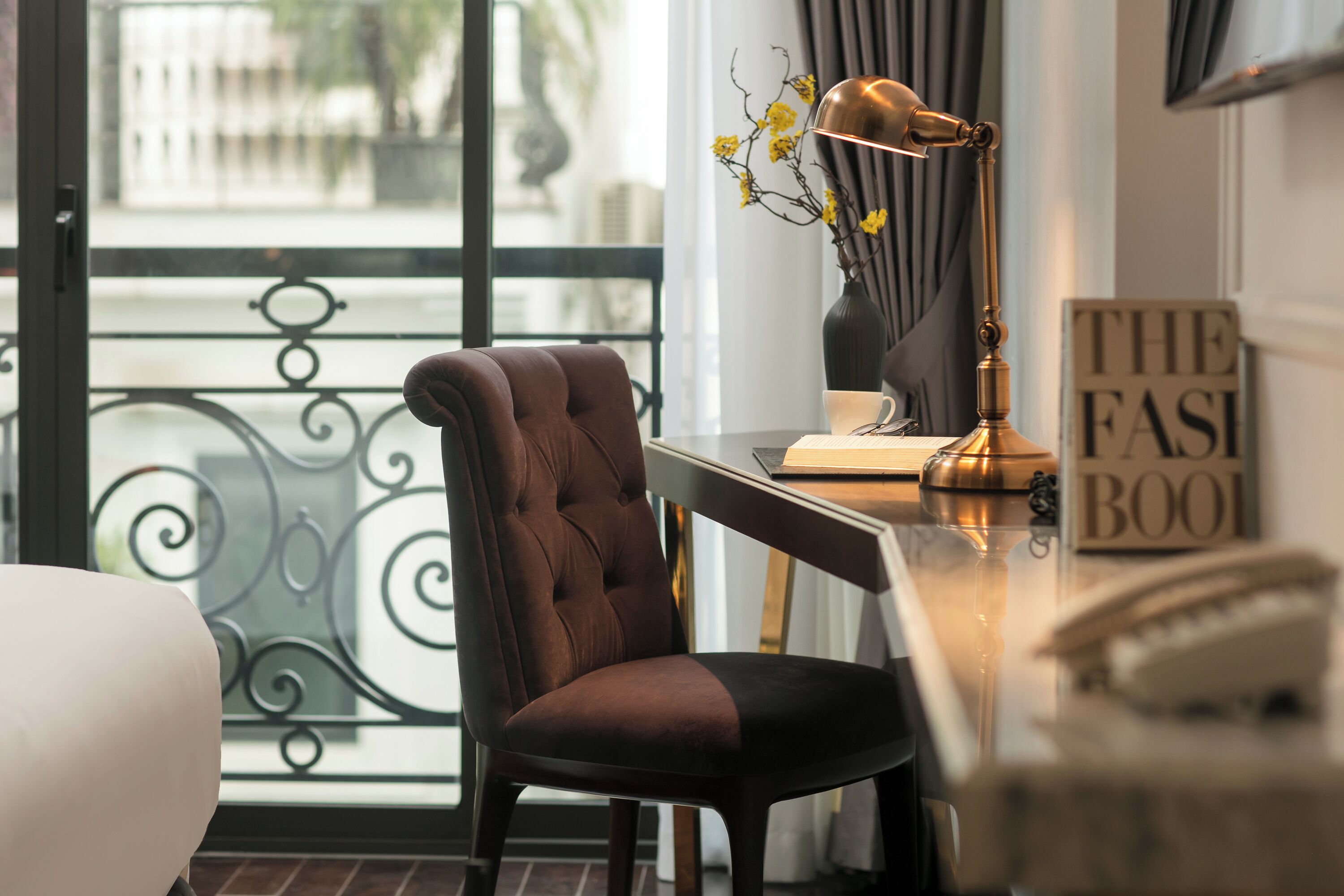 A modern room with a tufted chair, a desk with a lamp, and a view through a glass door.