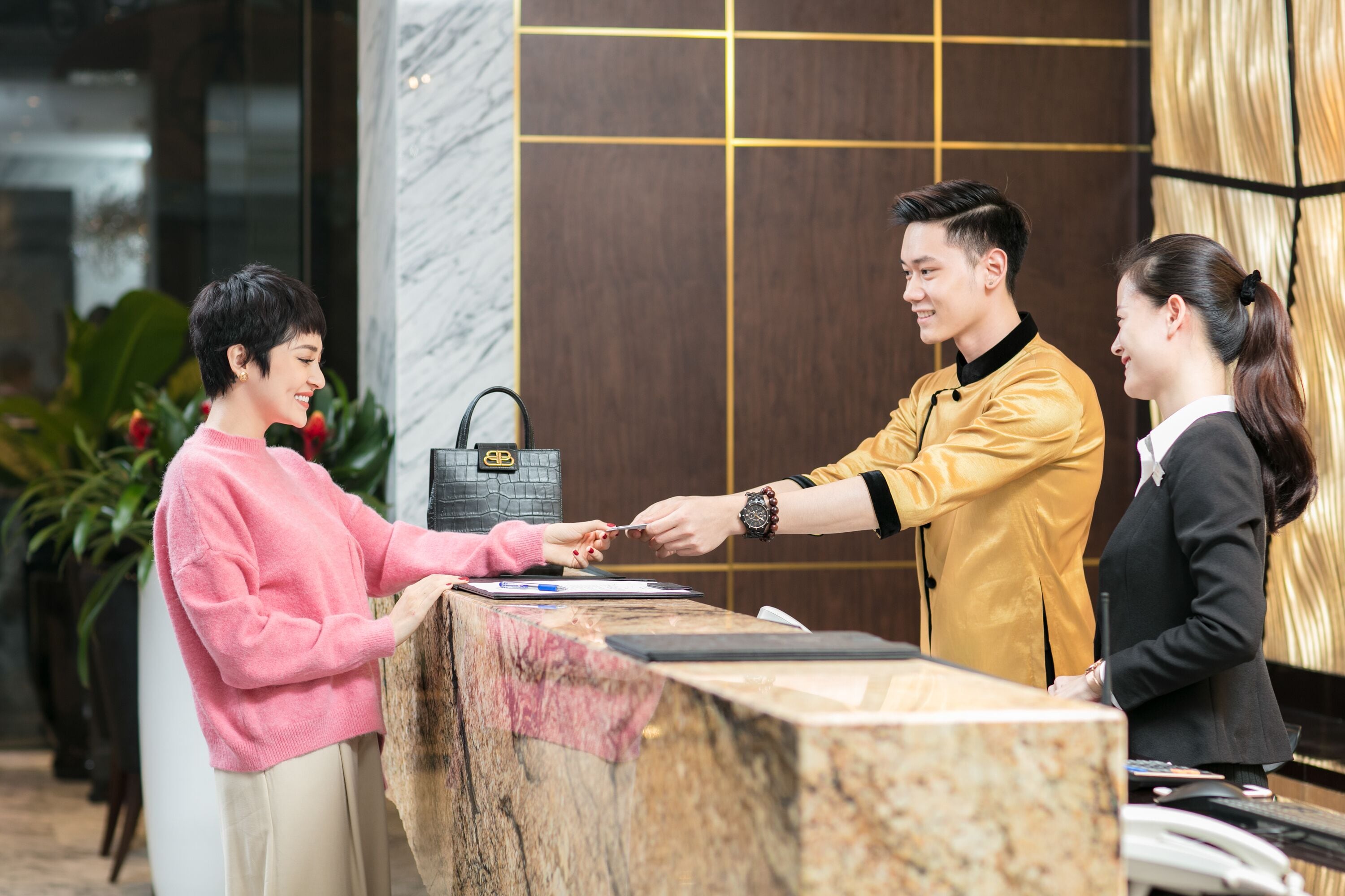 A reception desk with a marble top, a black handbag, and a person handing over a card.