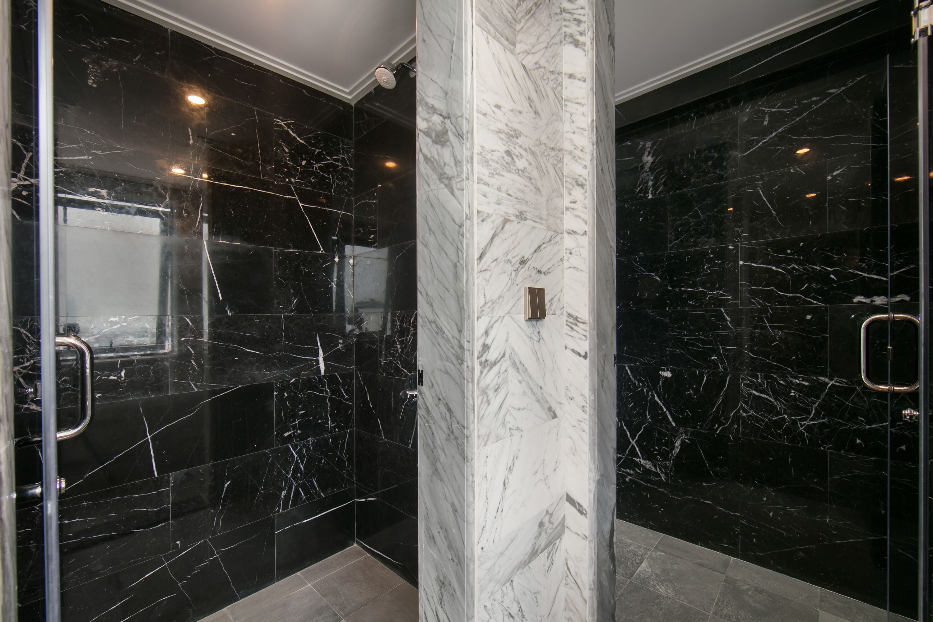 Un baño moderno con paredes de mármol negro y una columna central de mármol blanco.