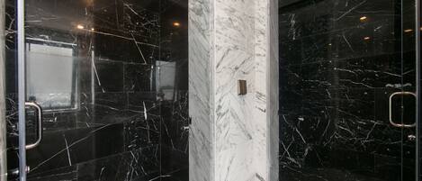 Un baño moderno con paredes de mármol negro y una columna central de mármol blanco.