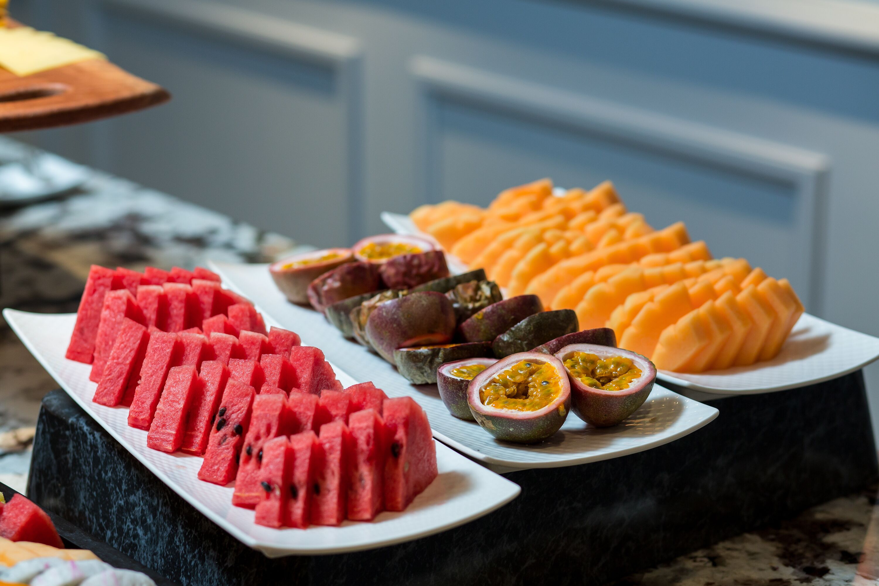 A buffet with watermelon, passion fruit, and cantaloupe arranged on plates.