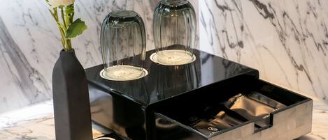 Uma toucador de banheiro com bancada de mármore, um vaso preto com flores brancas e dois castiçais de vidro.