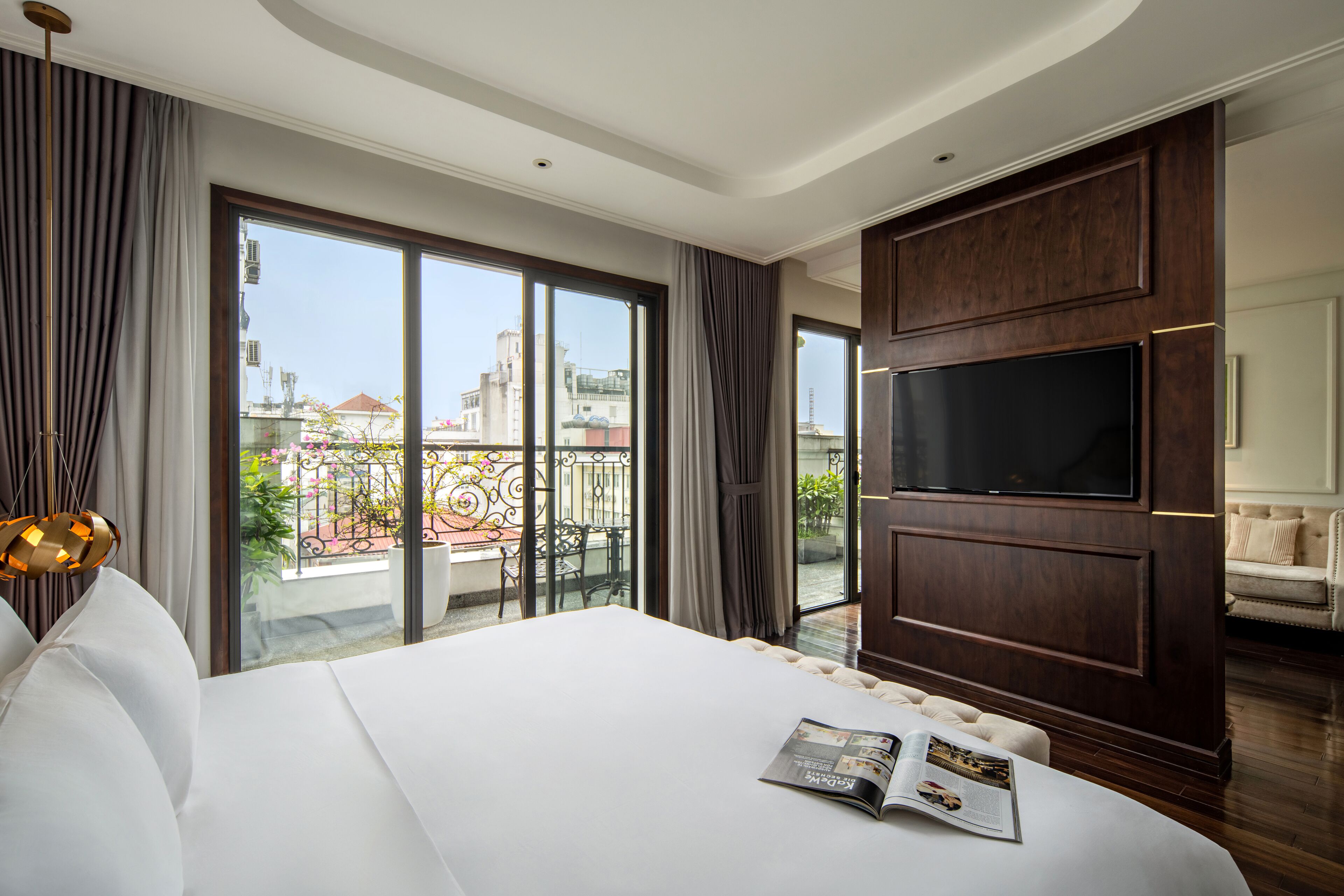 A hotel room with a large bed, a TV, and a balcony with a view of the city.