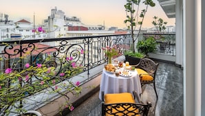 A balcony with a table set for breakfast, surrounded by potted plants and flowers. - Anatole Hotel Hanoi (Hanoi)
