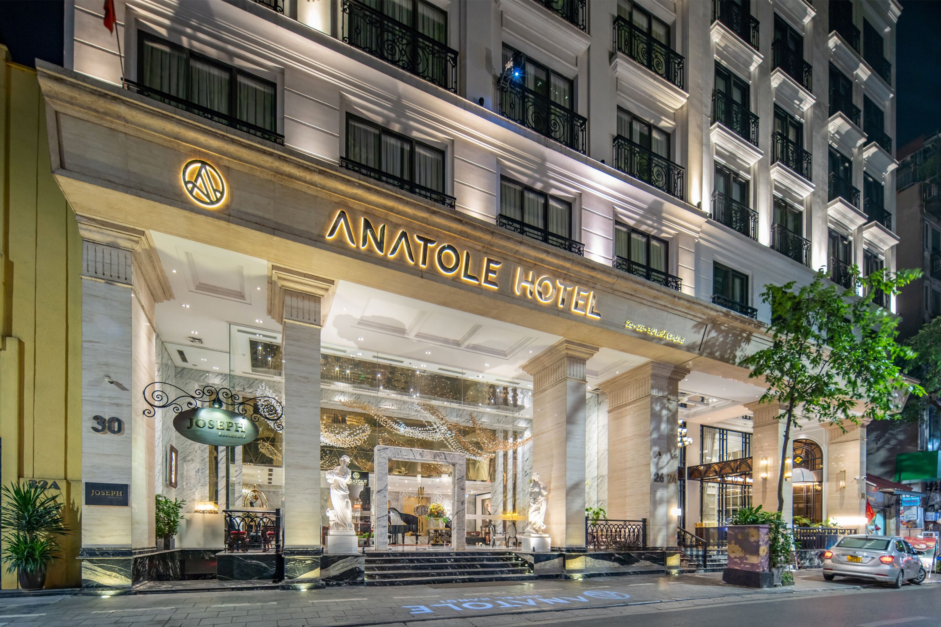 Exterior de l'Hotel Anatole, amb una entrada imponent, columnes de marbre i una façana ben il·luminada.
