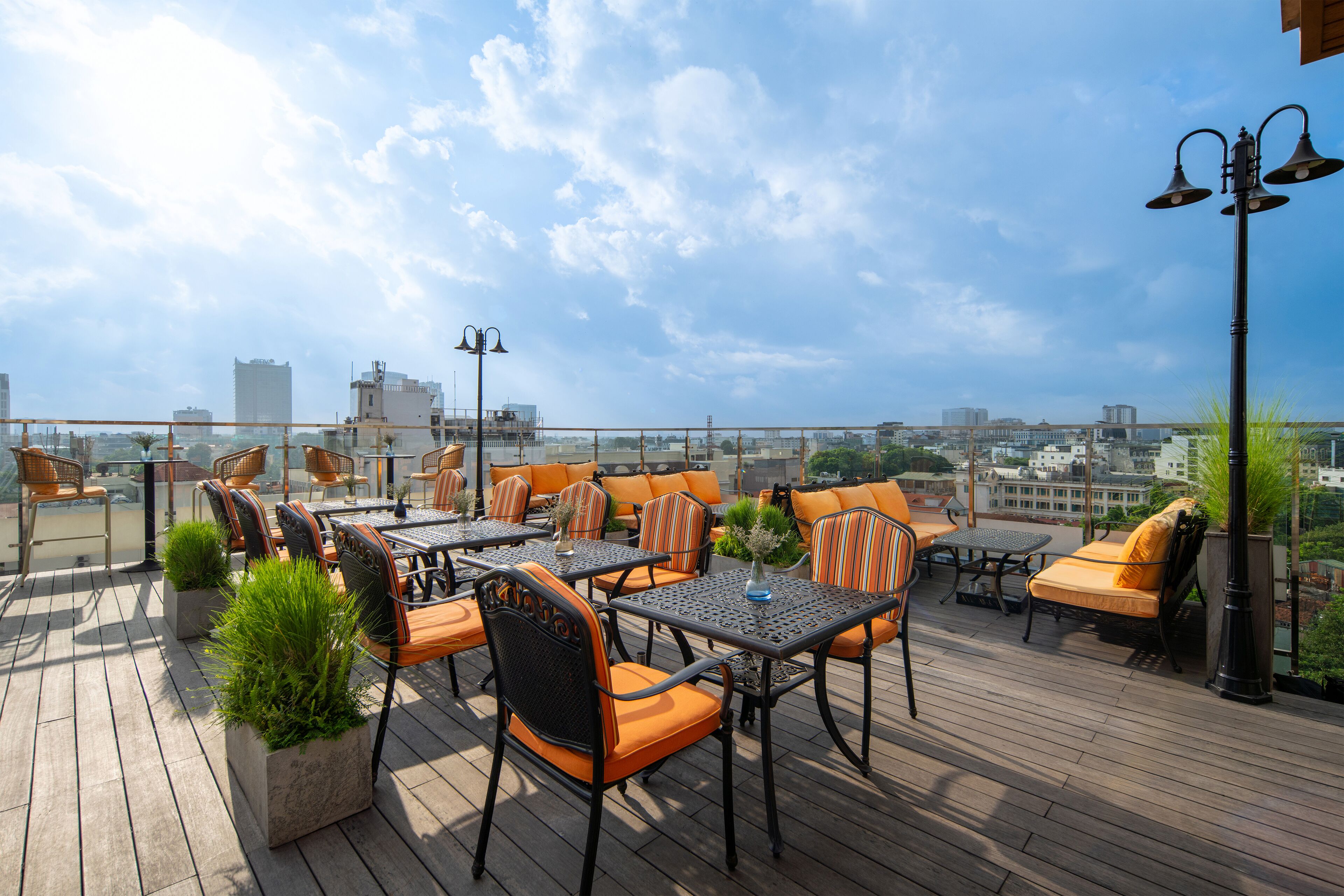 Terraza al aire libre con varias mesas y sillas, rodeada de plantas en macetas y vistas a la ciudad.