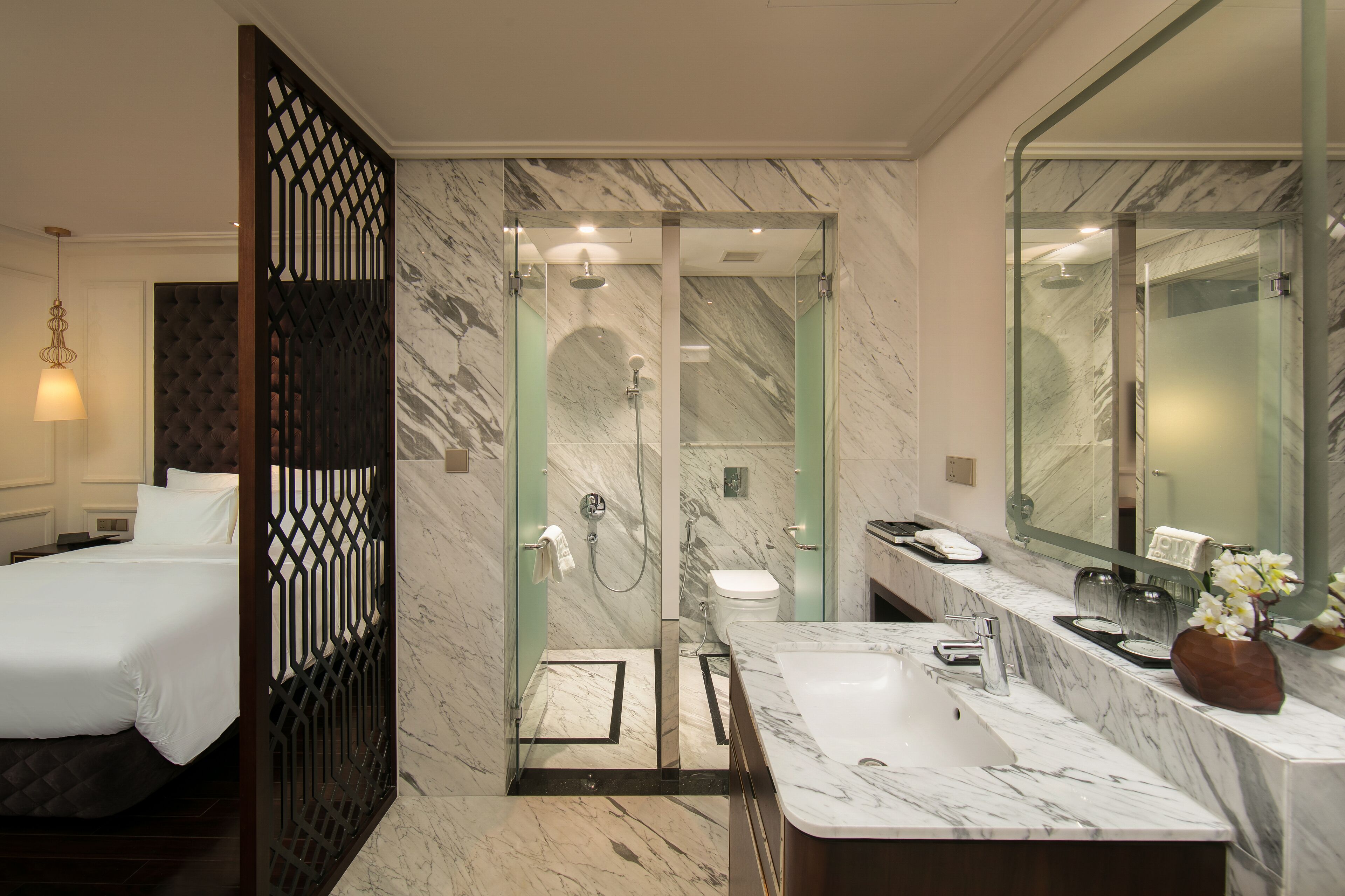 Un baño de hotel moderno con ducha de vidrio, lavabo de mármol y un espejo grande.