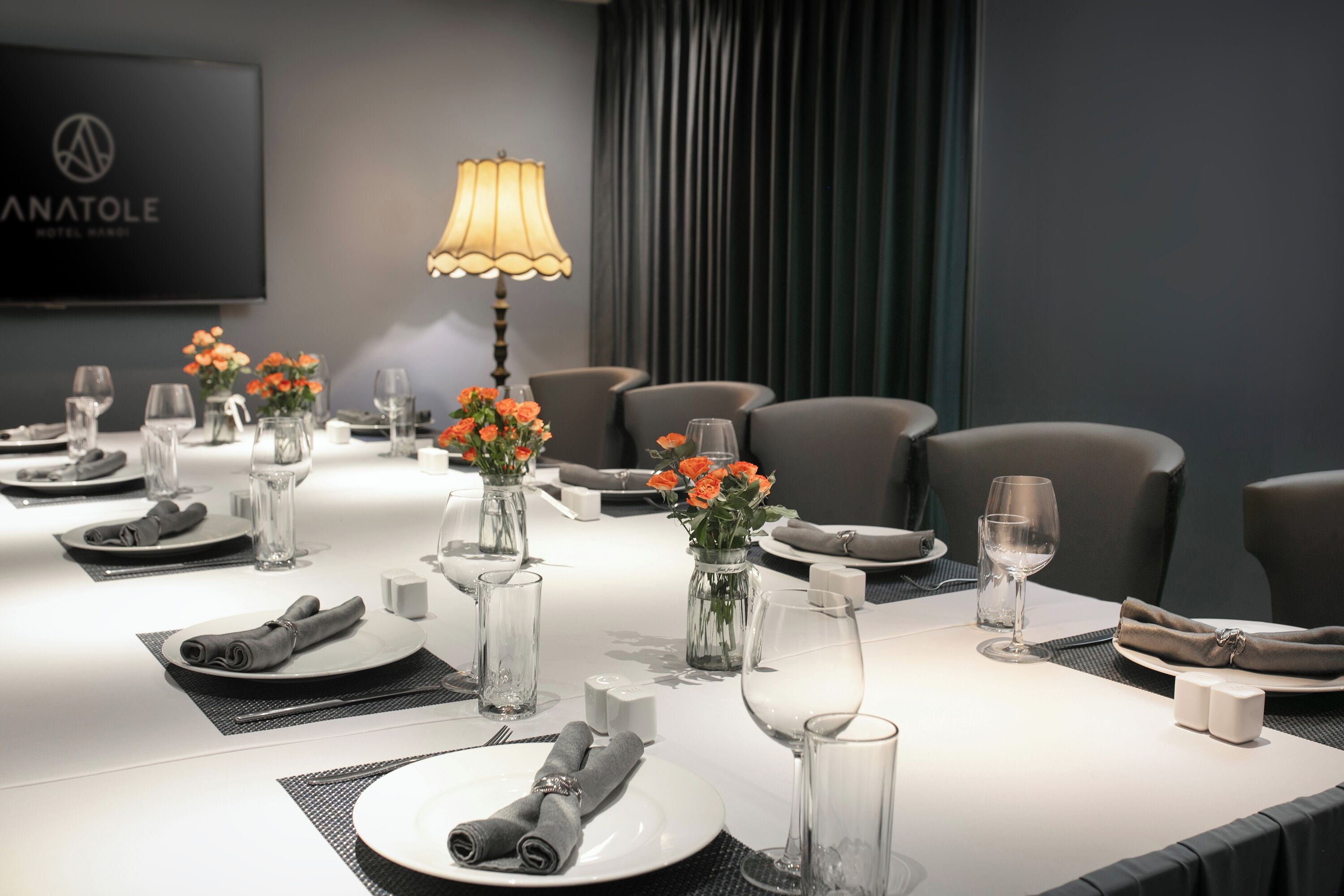 Een vergaderruimte met een lange tafel, gedekt voor een vergadering, voorzien van stoelen, een televisiescherm en een lamp.