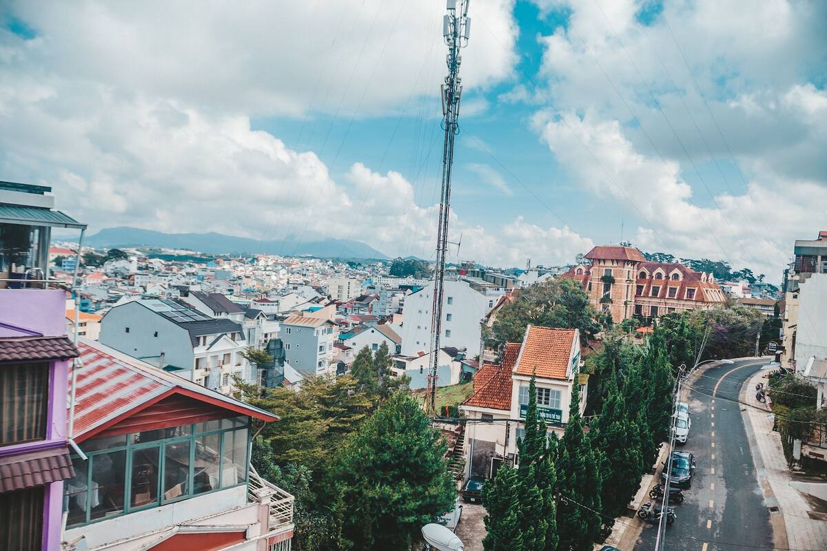 Um edifício alto com vários andares, uma antena destacada e vista para um horizonte urbano com diversos edifícios e uma montanha ao longe.