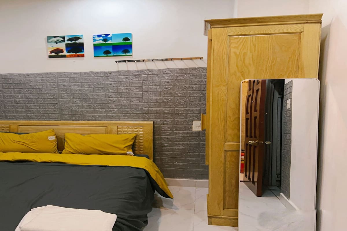 Quarto com uma cama, uma porta de madeira e duas obras de arte nas paredes.