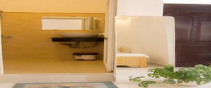 Une salle de bain avec une porte en bois, un lavabo, un miroir et un petit banc.
