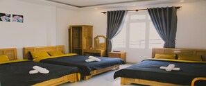 Une chambre d’hôtel avec trois lits en bois, chacun recouvert d’une couverture noire et jaune, et une armoire en bois.