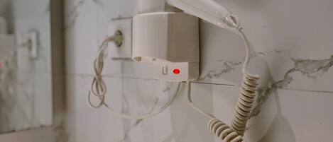 A hairdryer mounted on a wall with a marble pattern, connected by a coiled cord.