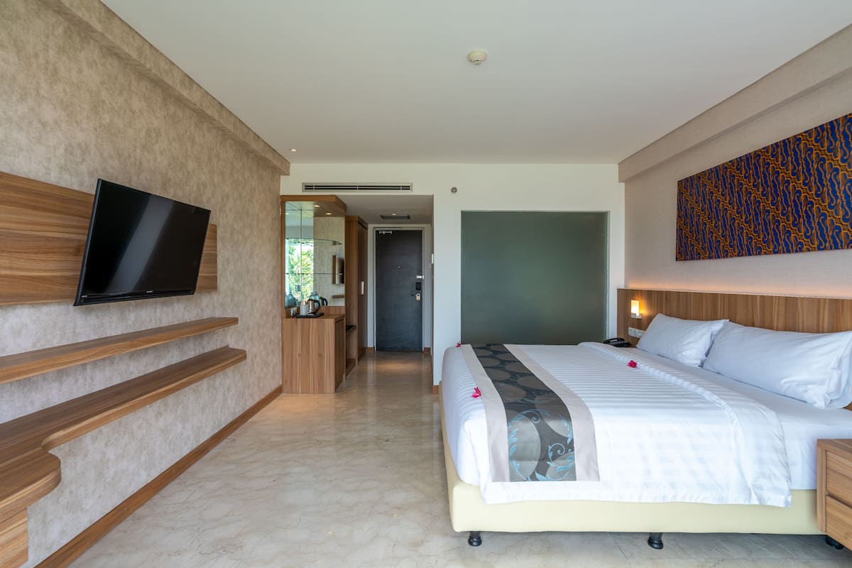 A modern hotel room with a large bed, a flat-screen TV mounted on the wall, wooden shelves, and a decorative wall piece.