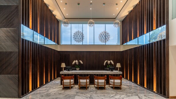 A modern lobby with a marble floor, a reception desk, and four wooden chairs. - The Capital Hotel and Resort Seminyak (Keroboken Kelod)