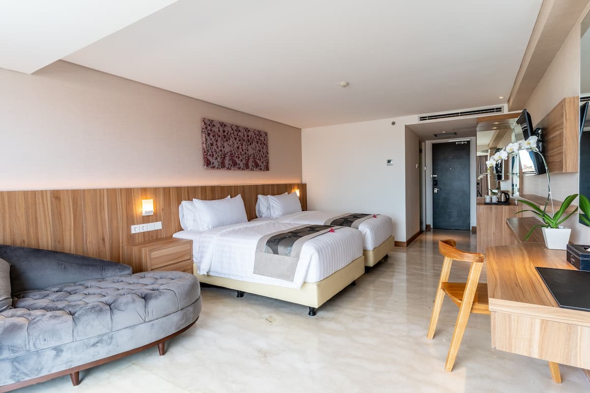 A modern hotel room with a large bed, a sofa, a desk, and a small potted plant.